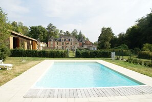 A rectangular swimming pool with a wooden deck, surrounded by a well-maintained lawn and a large brick building in the background. - Nettancourt Family Stay (Nettancourt)