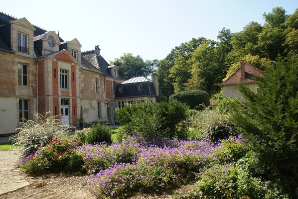 A historic building with a courtyard, surrounded by lush greenery and flowering plants. - Nettancourt Family Stay (Nettancourt)