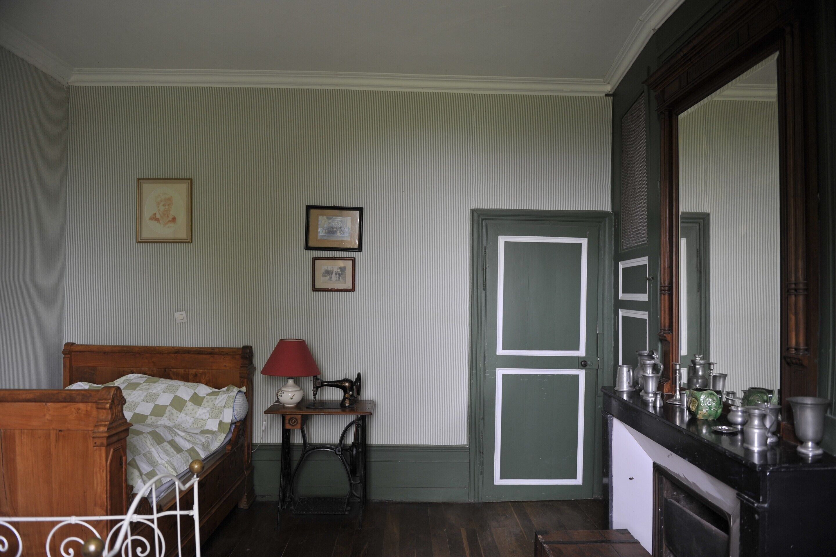 A room with a bed, a sewing machine, a mirror, and a door.