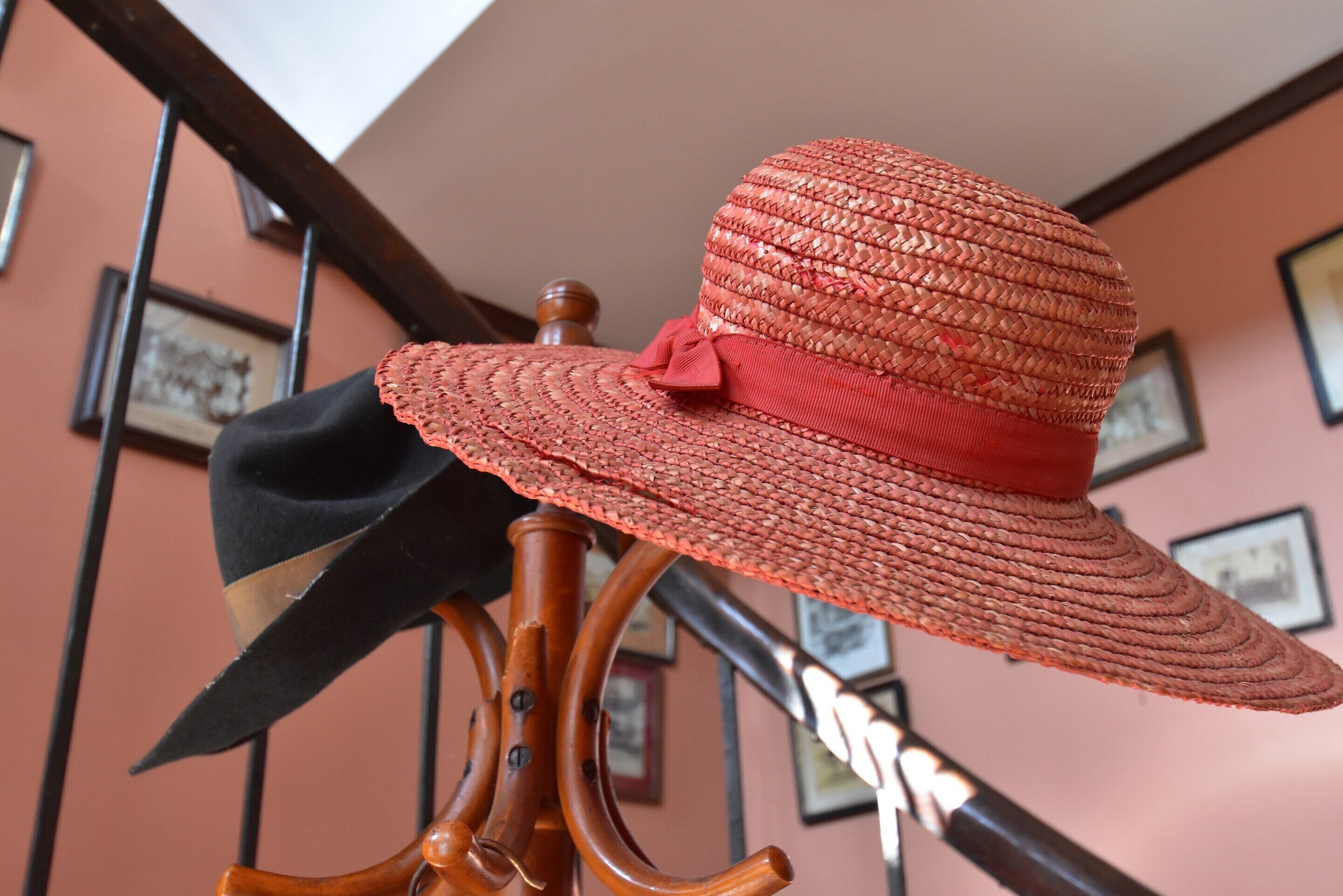 A hat on a wooden stand in a room with a staircase and framed pictures on the wall.