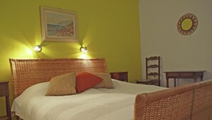 A bed with a woven headboard, a painting on the wall, and a small round mirror. - Villa in Cavalaire-sur-mer Near the Sea (Cavalaire-sur-Mer)