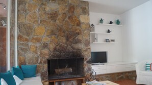 A living room with a stone fireplace, white furniture, and a television on a white cabinet. - Villa in Cavalaire-sur-mer Near the Sea (Cavalaire-sur-Mer)