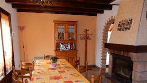 Een eetgedeelte met een lange tafel, stoelen, een kast en een open haard.