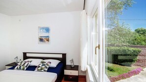 A bedroom with a bed, bedside tables, a nightstand, a window with curtains, and a view of greenery outside. - Spacious Holiday Home With Private Pool (Polaca)