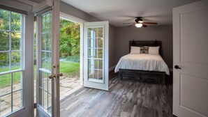 A bedroom with a bed, a ceiling fan, and a view of a garden through open doors. - Niagara Wine Routes Fifth street (St. Catharines)