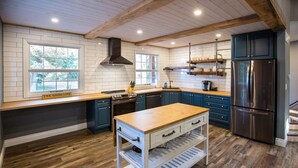 A modern kitchen with wooden flooring, a central island, dark blue cabinets, and a stainless steel refrigerator. - Niagara Wine Routes Fifth street (St. Catharines)