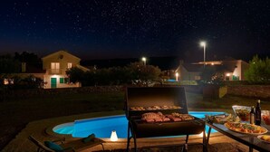 A backyard with a swimming pool, a barbecue grill, and a dining table set for an outdoor meal.