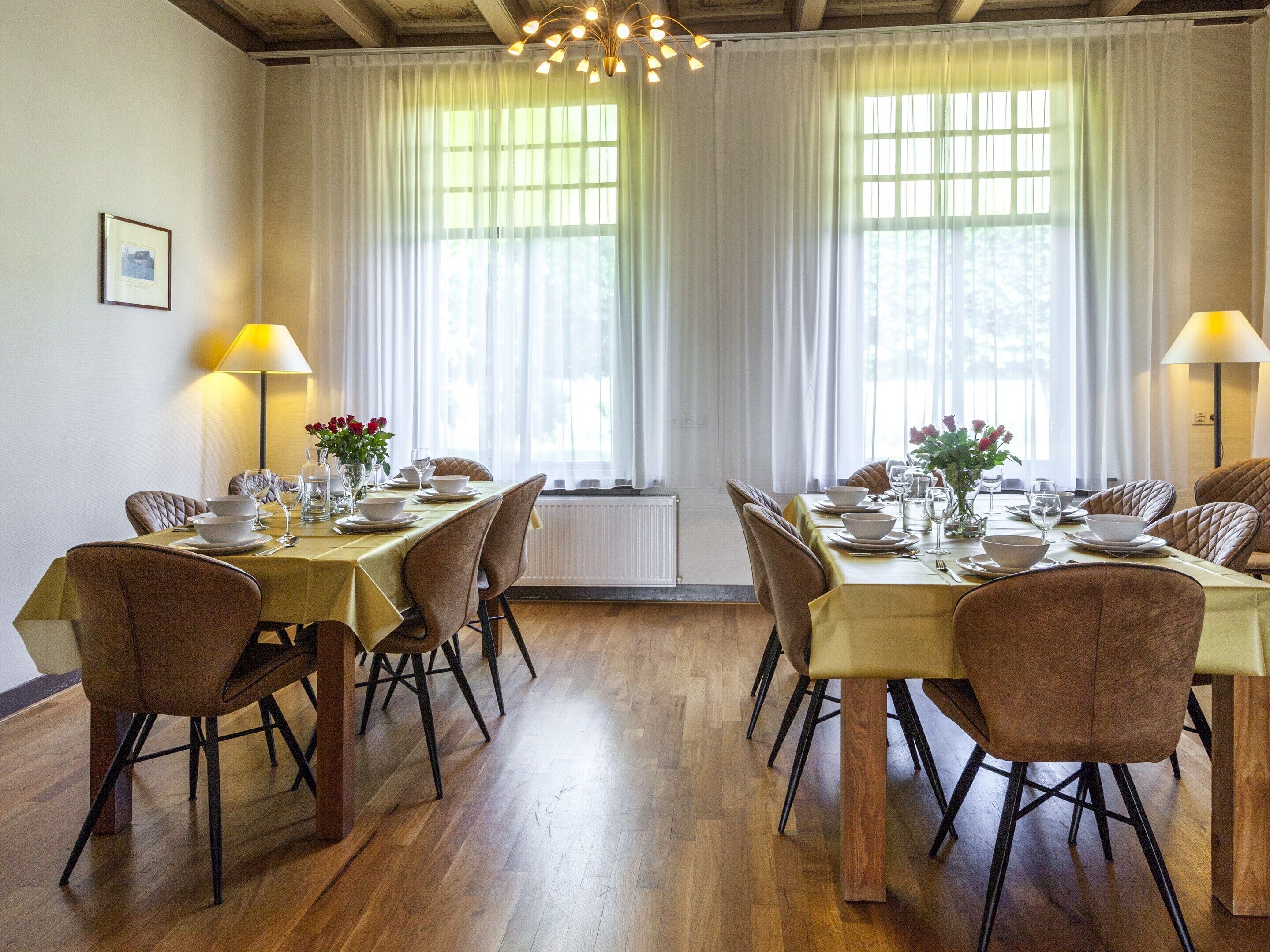 Une salle à manger avec un plancher en bois, une table dressée pour quatre personnes et deux lampes.