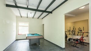Una habitación con mesa de billar, equipo de ejercicio y una ventana con luz natural.