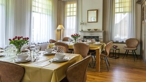 Comedor con una mesa dispuesta para cuatro, chimenea y ventanas grandes con cortinas.