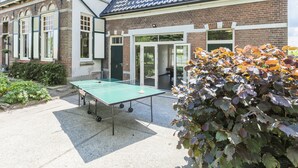 Un patio con mesa de ping pong, un edificio de ladrillo con tejado de baldosas y una puerta verde.
