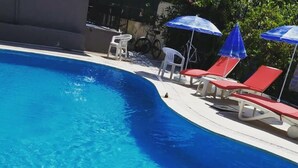 Una piscina azul cristalina con sillas de descanso rojas y sombrillas azules.