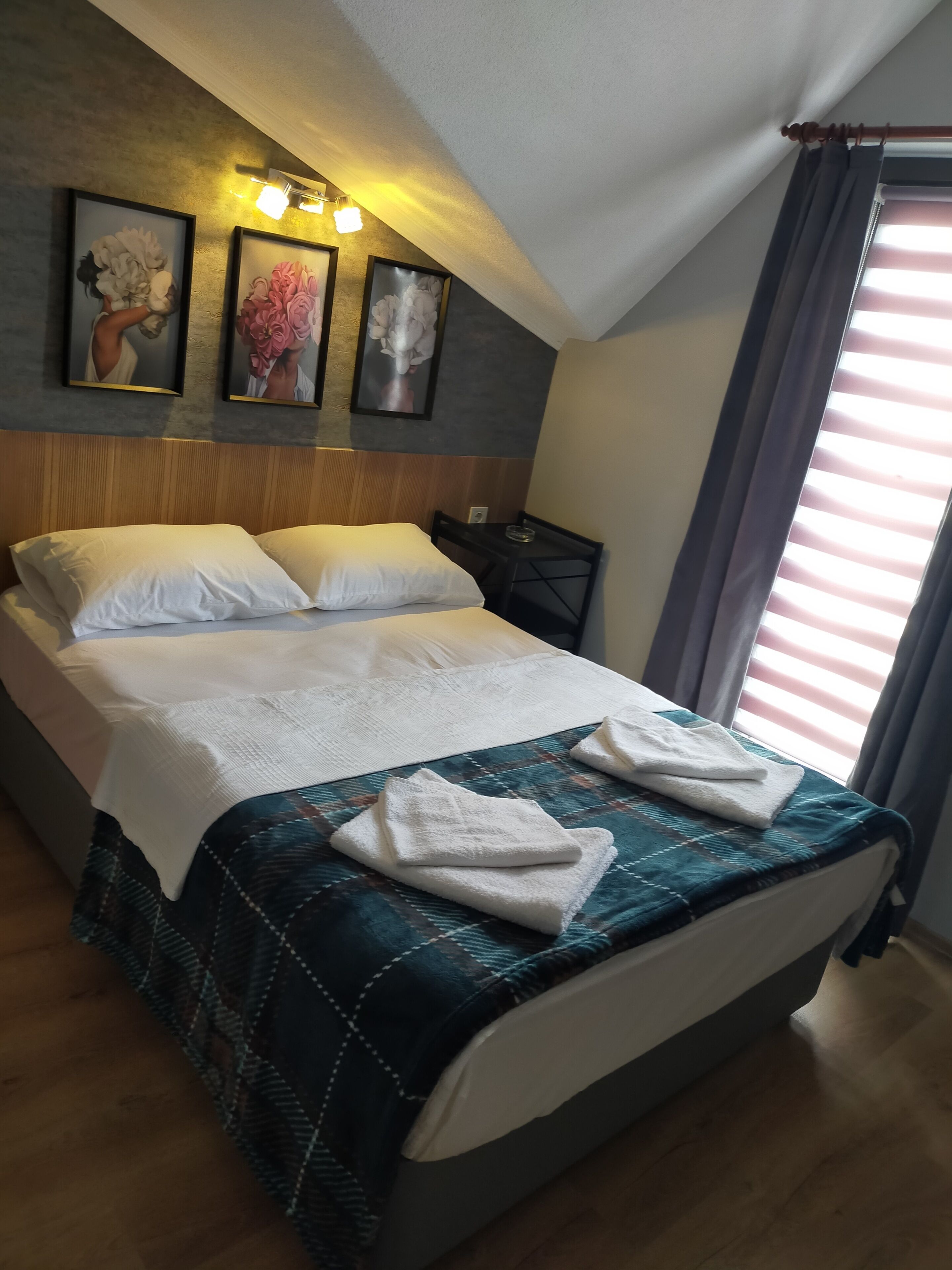 A neatly made bed with a blue and white patterned bedspread, white pillows, and two folded white towels on the bed. There are three framed artworks on the wall above the bed.