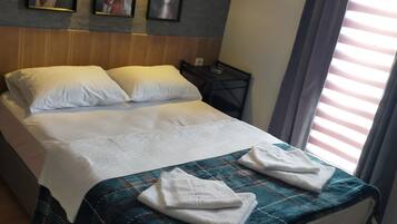A neatly made bed with a blue and white patterned bedspread, white pillows, and two folded white towels on the bed. There are three framed artworks on the wall above the bed.