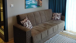 Una sala de estar moderna con un sofá, un cuadro de un paisaje costero, una lámpara de pared y una alfombra estampada.