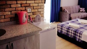 Habitación de hotel compacta con kitchenette, cama con cubrecama escocés, sofá y cortina azul.