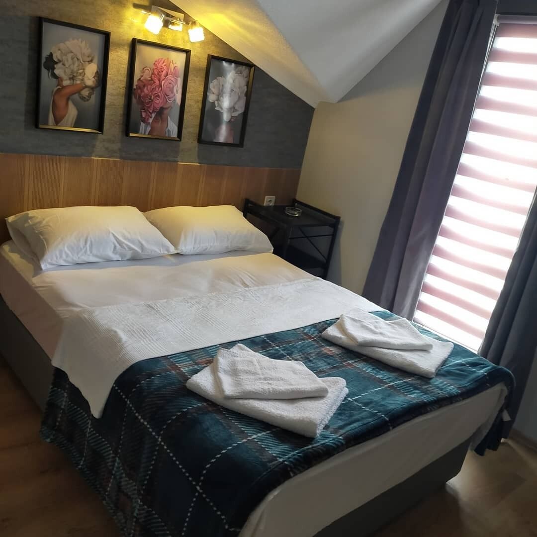 A neatly made bed with white linens and a blue quilt, a wooden headboard, and three framed pictures on the wall.