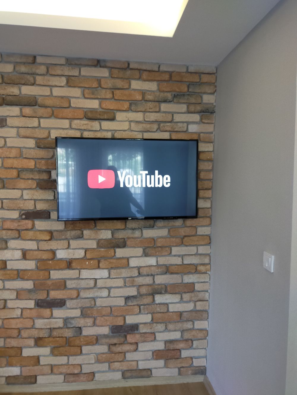 A flat-screen TV mounted on a brick wall with a YouTube logo displayed.