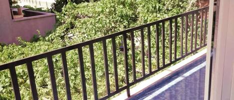 A balcony with a metal railing, a view of greenery and buildings in the background.