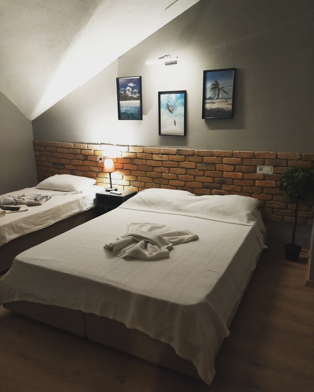 Ein Zimmer mit zwei Betten, einem Ziegelstein-Kopfende, einem Nachttisch mit Lampe und gerahmten Bildern an der Wand.