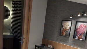 Habitación de hotel con cama, una mesita, una silla, baño visible a través de una puerta abierta y dos cuadros en la pared.