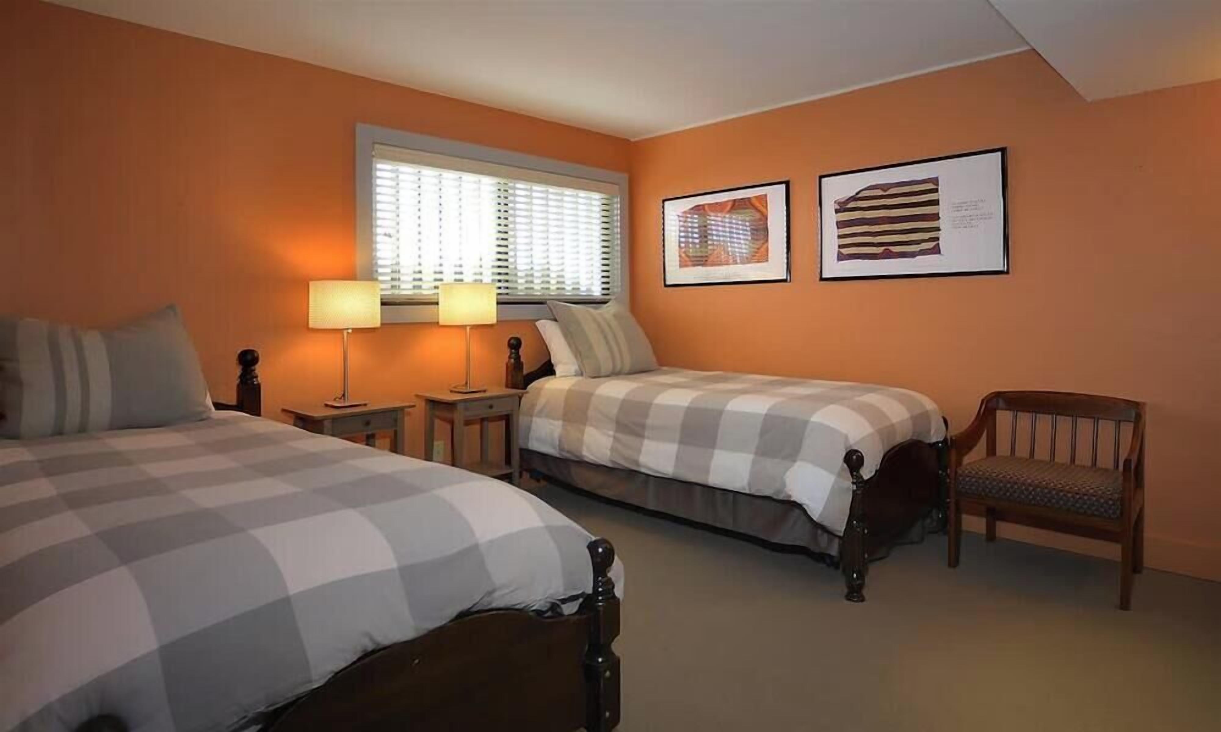 A bedroom with two beds, a nightstand, a chair, and two framed pictures on the wall.