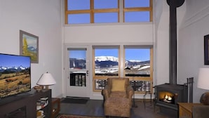 Un salon doté d’une cheminée, d’un téléviseur et d’une grande fenêtre offrant une vue sur les montagnes.