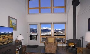 A living room with a fireplace, a television, and a large window with a mountain view.