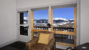 Une pièce avec un canapé, une lampe et une vue sur des montagnes enneigées, visible à travers de grandes fenêtres.