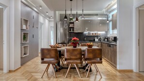 Een moderne keuken met een centraal eiland, hanglampen en een eethoek met een houten tafel en lederen stoelen.