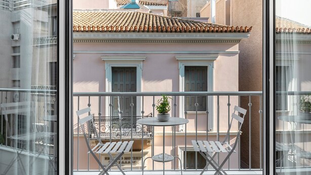 Een balkon met uitzicht op omliggende gebouwen, een tafeltje met stoelen en een bloempot.