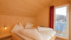A wooden cabin bedroom with two beds, a window with a red curtain, and a view of a snowy landscape. - Chalet in Hohentauern Near Ski Lift (Hohentauern)
