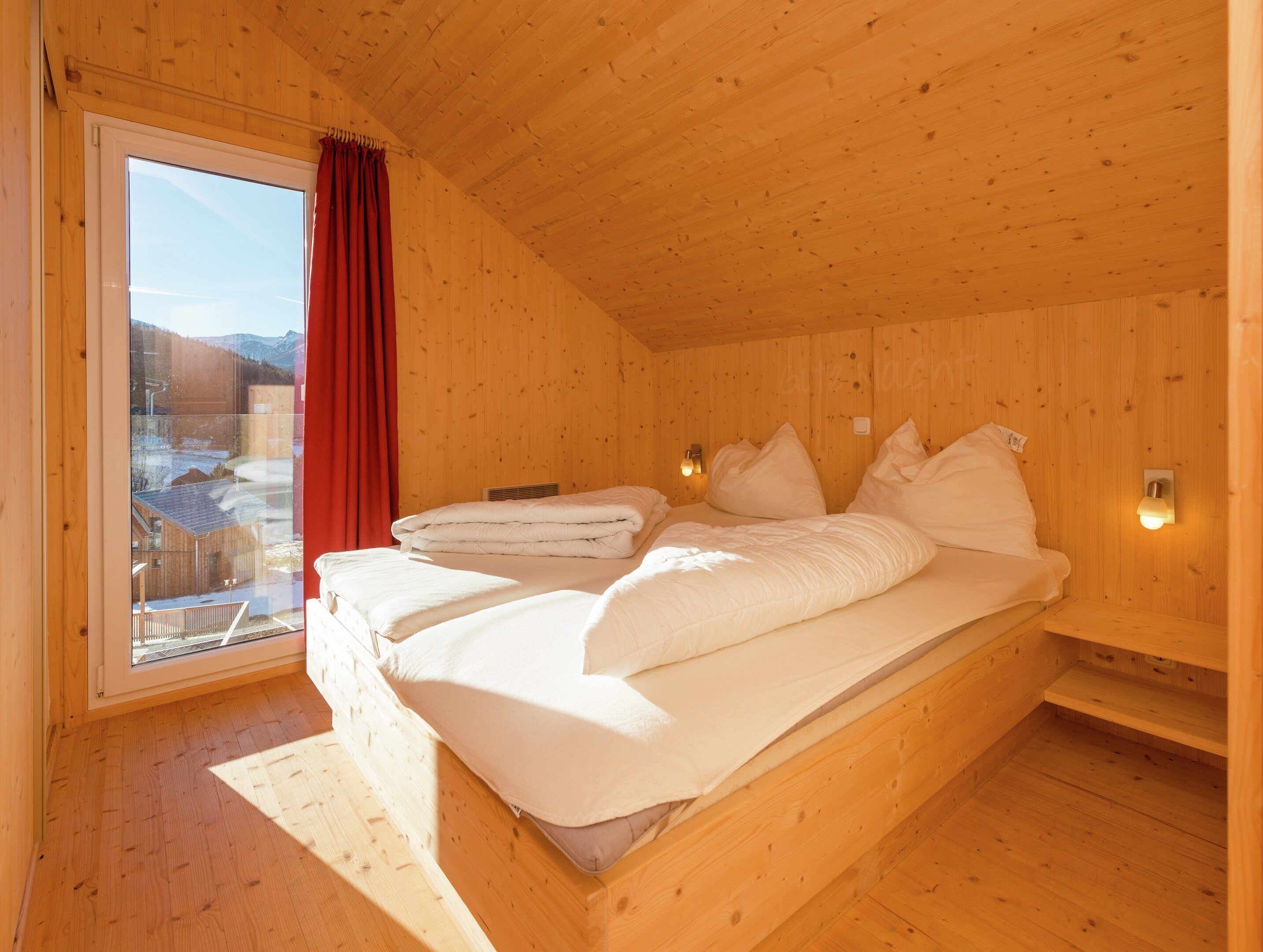 A wooden cabin bedroom with a bed, window, and a view of a snowy landscape.