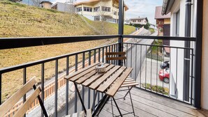 A balcony with a wooden table and benches, overlooking a residential area with houses and a road.