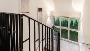 A modern staircase with black railings and a view of a green landscape through large windows.