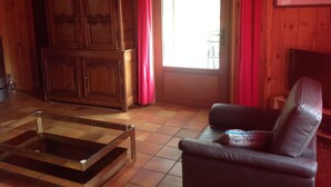 Un intérieur en bois avec une table basse en verre, un canapé en cuir et une porte ornée de rideaux rouges.