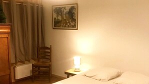 Une chambre à coucher avec un lit, une chaise, une table de chevet avec une lampe, un radiateur et un tableau accroché au mur.