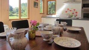Un coin repas avec une table en bois dressée pour quatre personnes, entourée de vaisselle à motifs et d’un vase contenant une fleur rose.