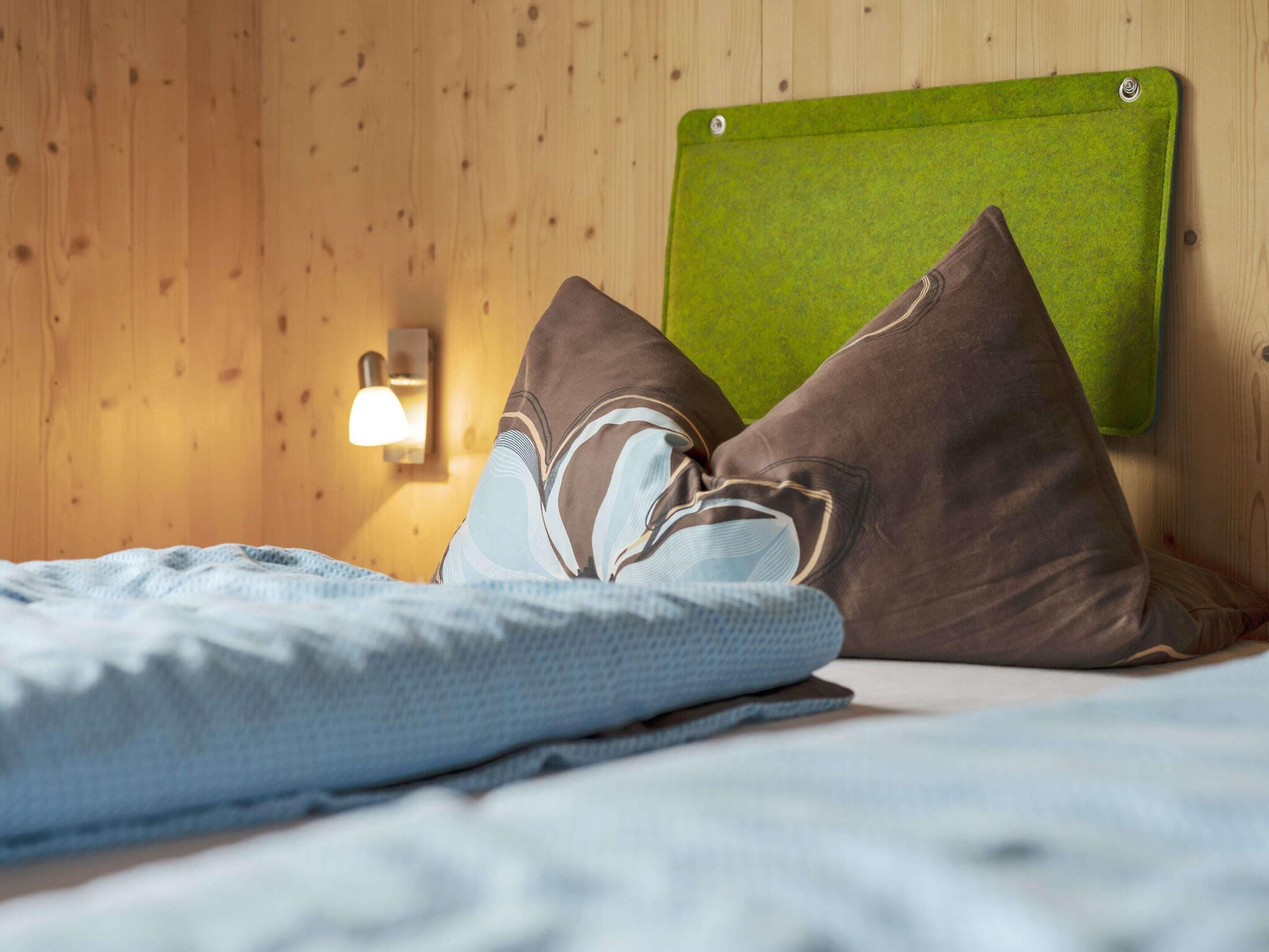 Una cama bien hecha con cabecera verde, dos almohadas y una lámpara de noche.