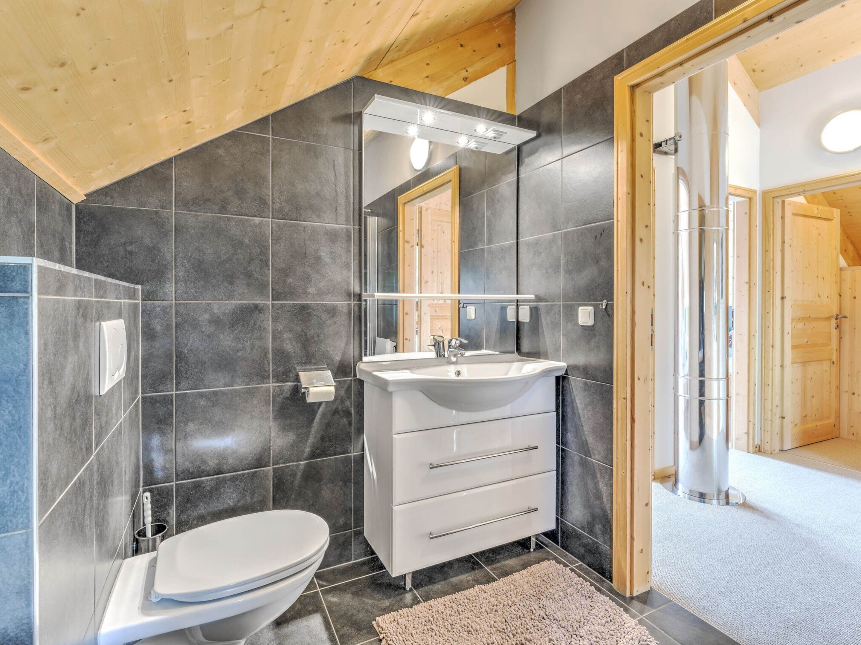 Un baño moderno con un lavabo blanco, un inodoro y paredes con azulejos oscuros.