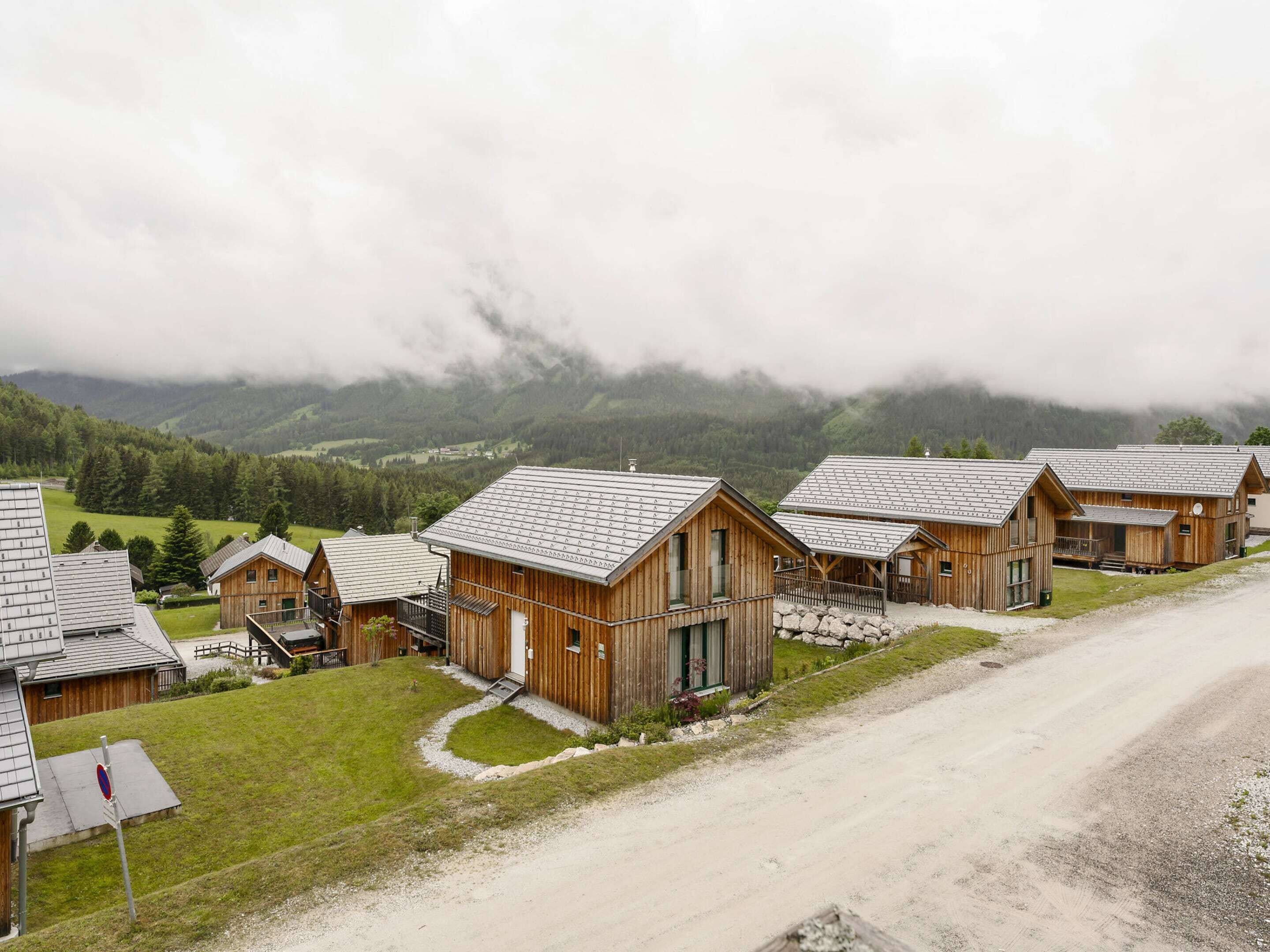 A row of wooden cabins with a gravel driveway, set against a mountainous backdrop.