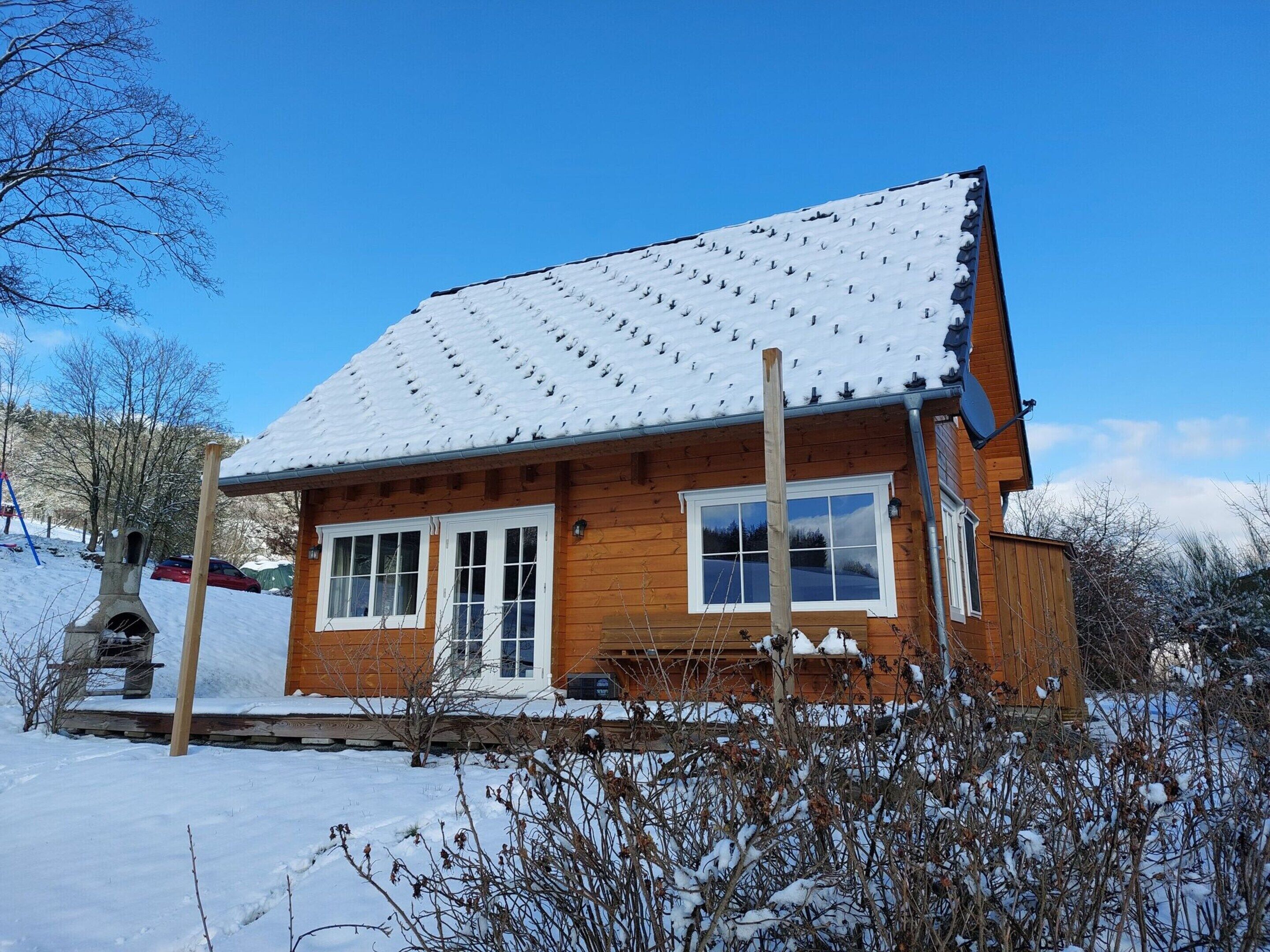 A wooden cabin with a snow-covered roof, windows, and a chimney.