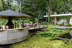 A rustic gazebo with a chimney, a wooden deck, and a pond with lily pads.