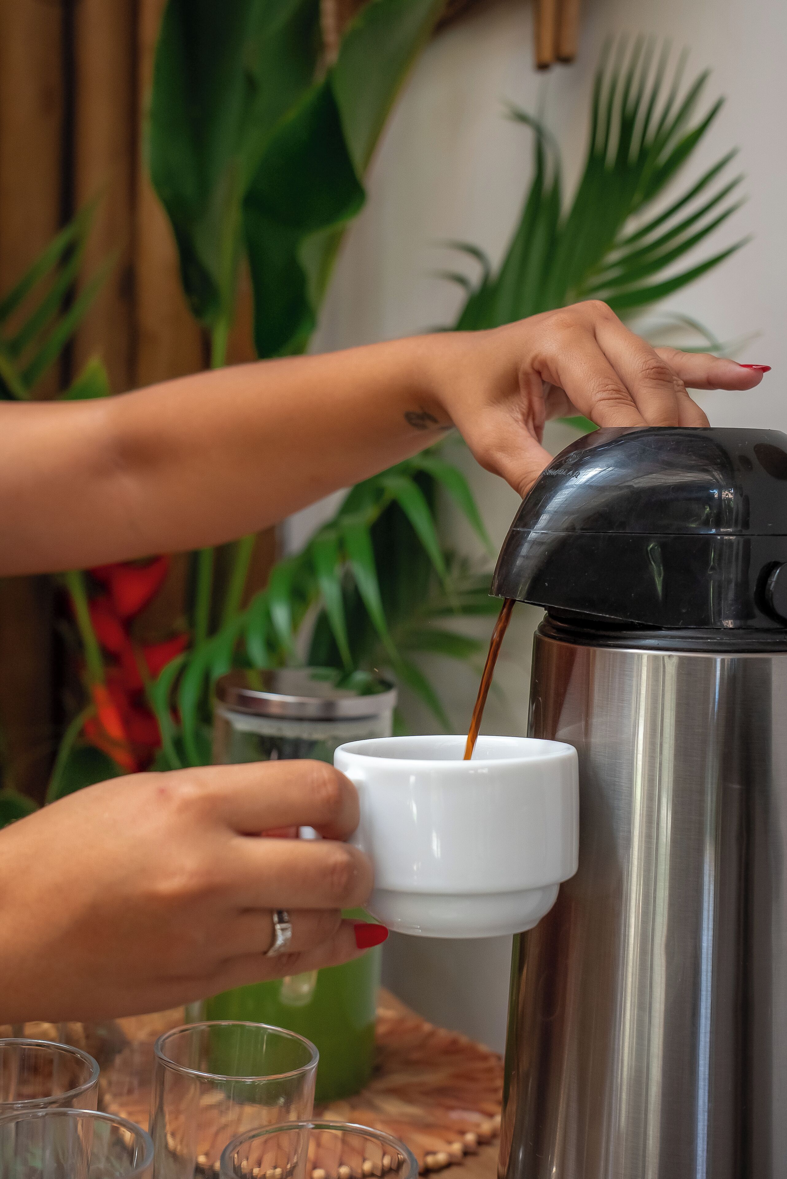 A person pouring coffee from a coffee maker into a cup.