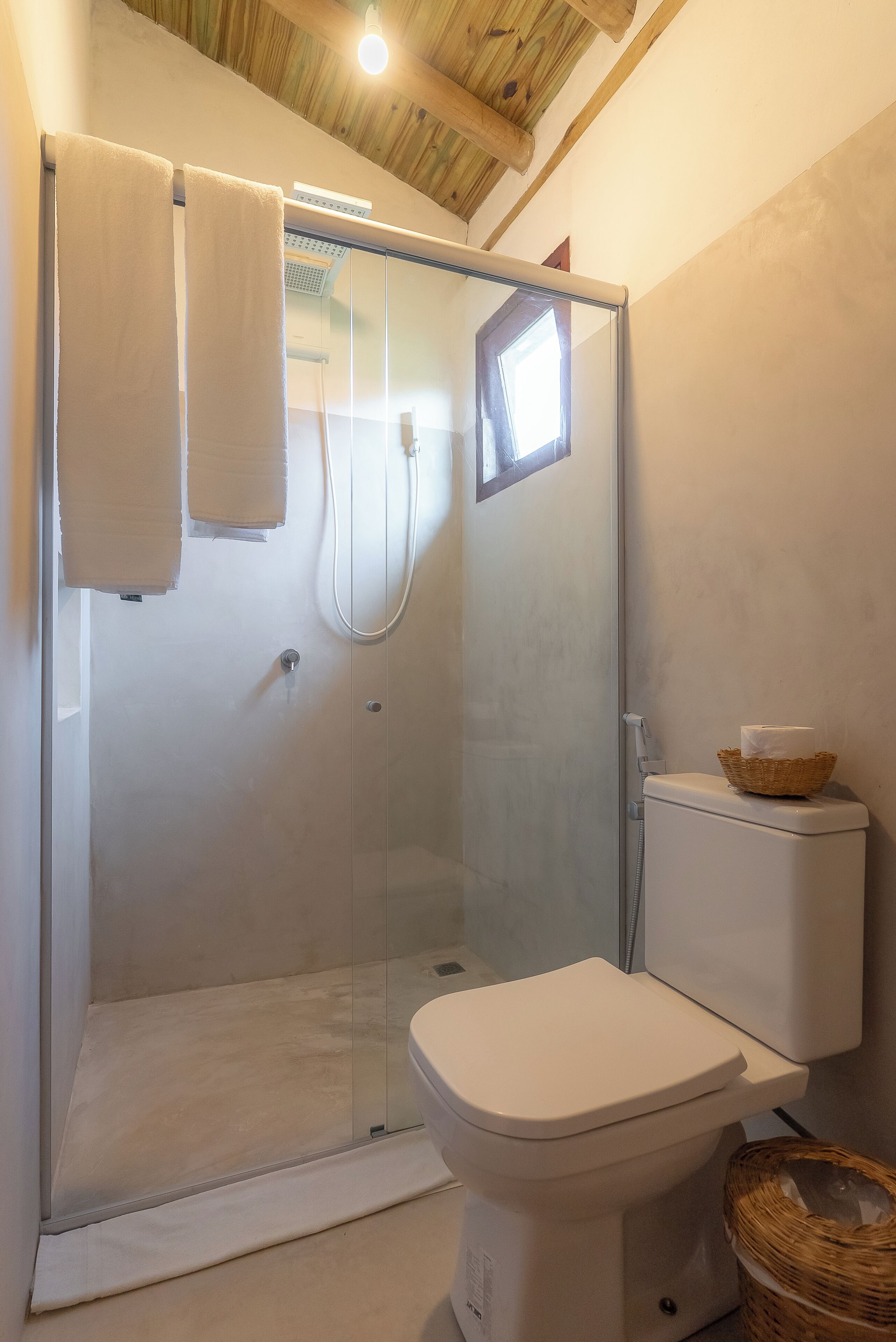A bathroom with a glass-enclosed shower, a white toilet, and a wicker basket on the floor.