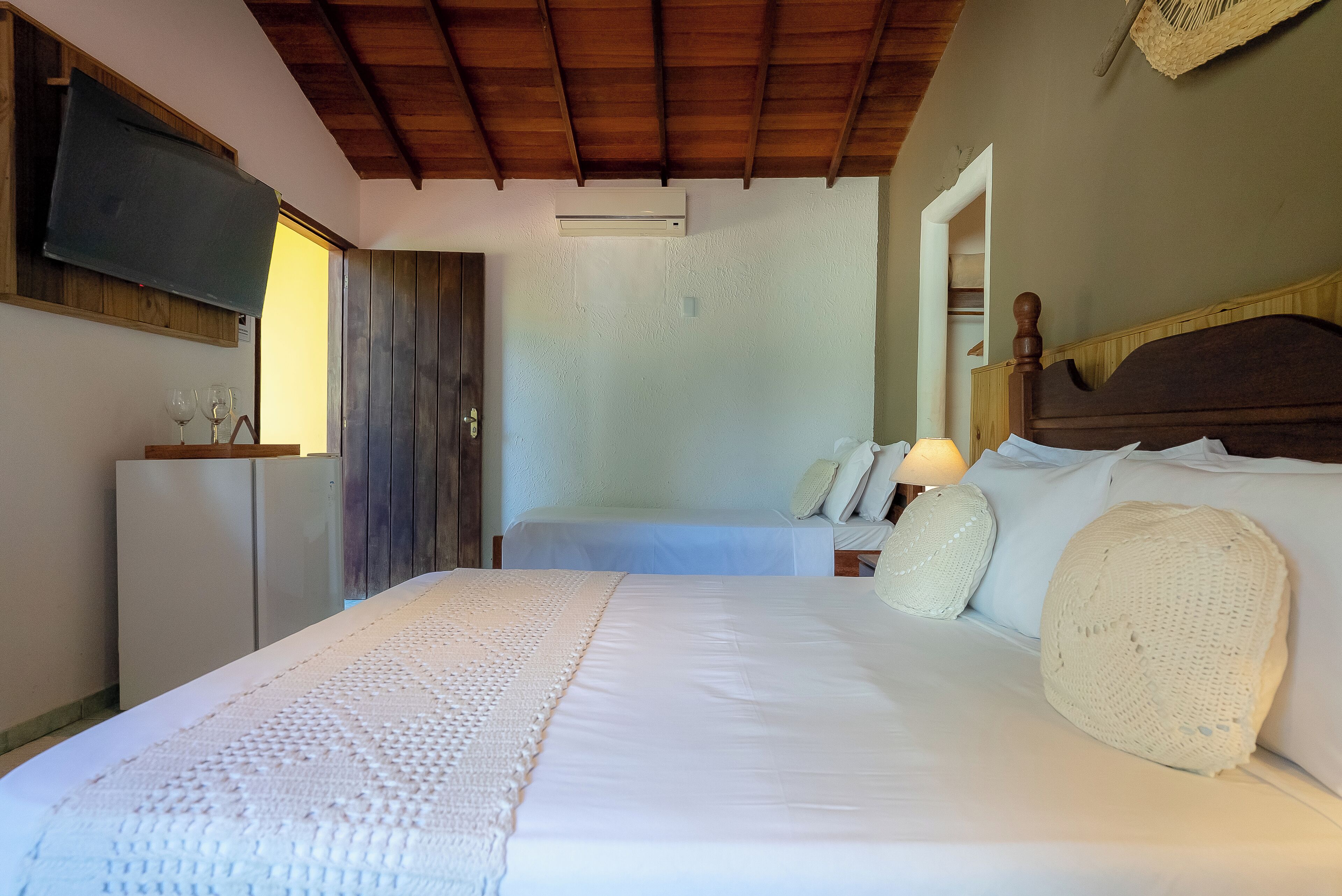 Un dormitorio con una cama grande, un televisor instalado en la pared y techo de madera.