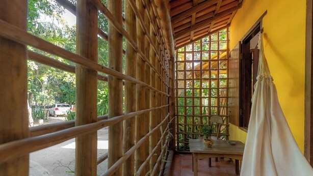 A covered balcony with wooden railings, a table with chairs, and a view of greenery outside. - Pousada Por do sol (Porto Seguro)