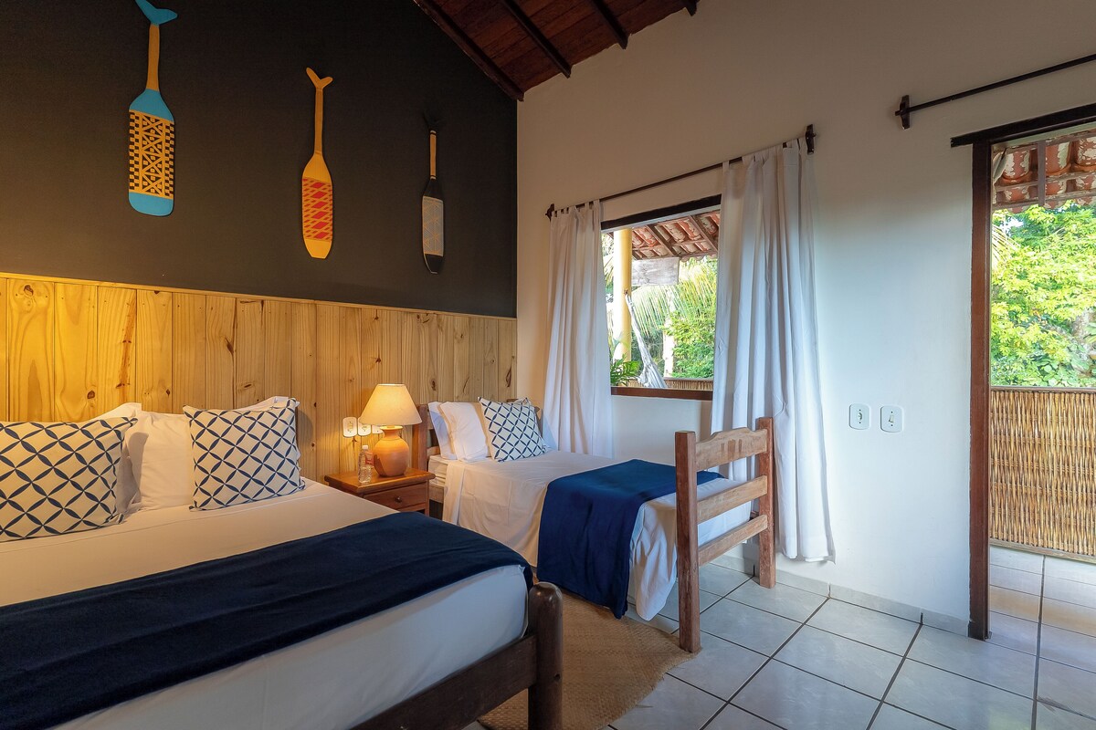 A bedroom with two beds, wooden headboard, white bedding, patterned pillows, and a window with white curtains.