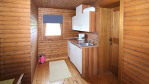 Eine kleine Küche mit Holzwänden, einem Fenster mit blauer Jalousie, einer Spüle, einer Kaffeemaschine und einem Mülleimer.