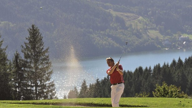 Ein Golfer auf einer Grünfläche mit einem See und Bäumen im Hintergrund.